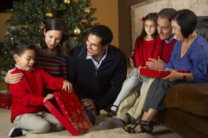 Multi Generation Family Opening Christmas Presents In Front Of Tree