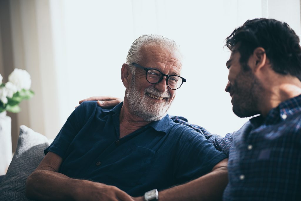 happy adult son and senior father laughing on sofa at home